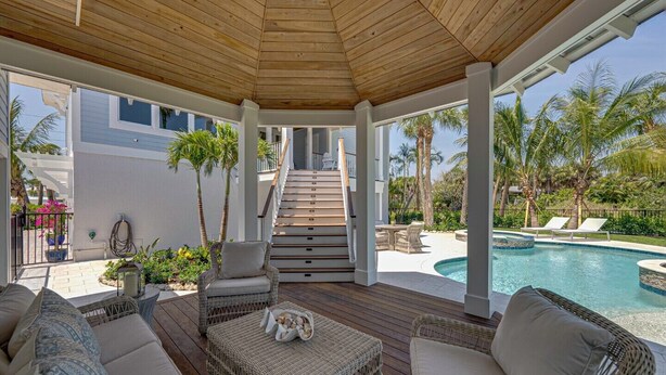 A covered outdoor area with a pool, wicker furniture, and a staircase leading to a second floor.