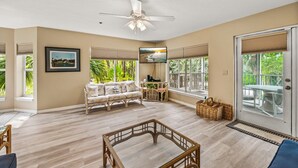 A spacious living area with a ceiling fan, a sofa, a glass coffee table, and a view of the outdoors through large windows. - 2740 Shore Ln - 1 block to the peach - Pet Friendly!  Large Home (Boca Grande)