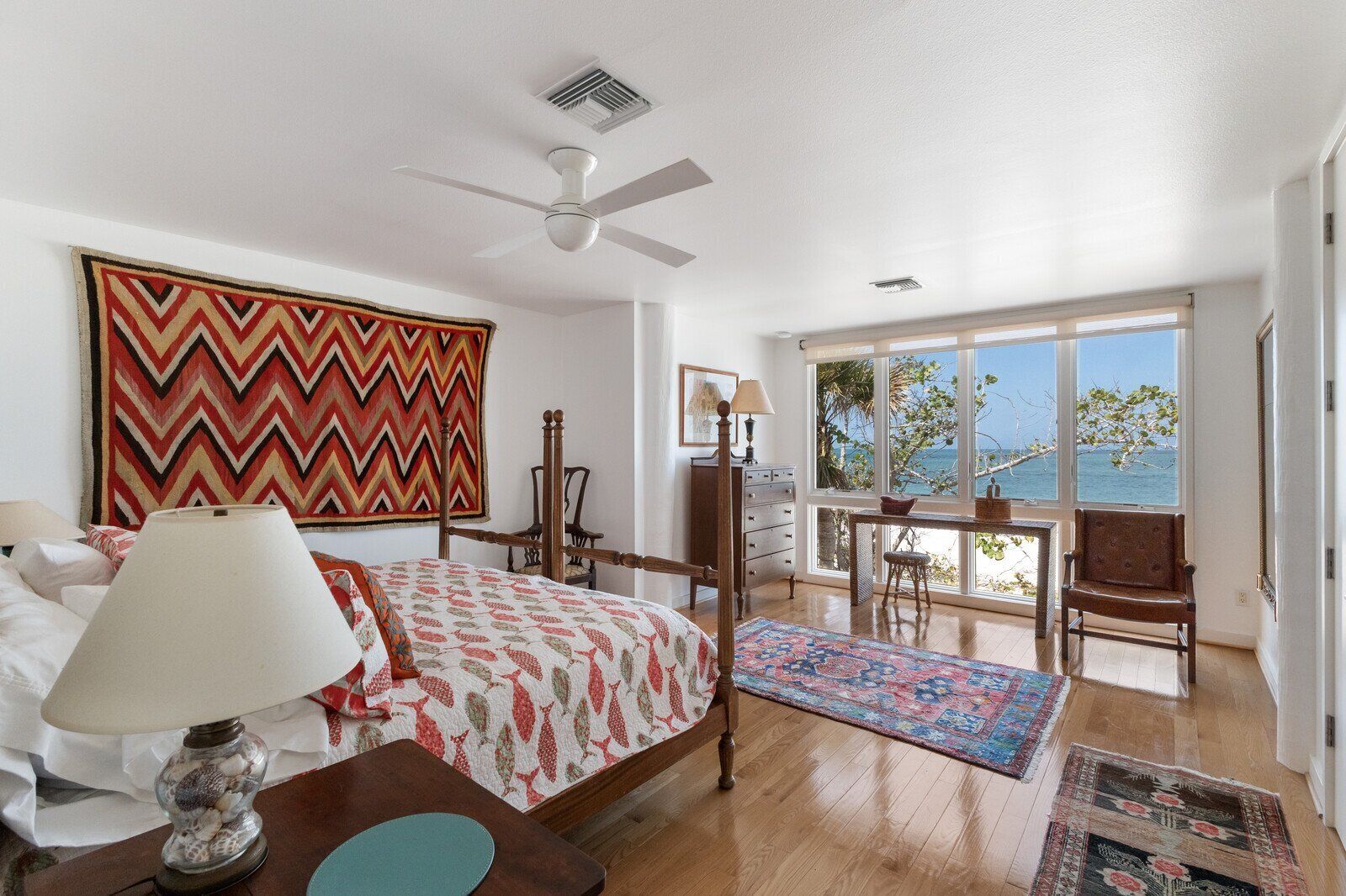 A bedroom with a bed, a desk, a chair, and a view of the sea.