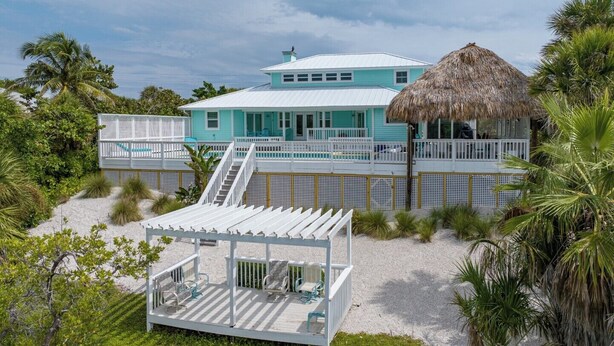 A two-story beach house with a thatched roof, a covered deck, and a pool.