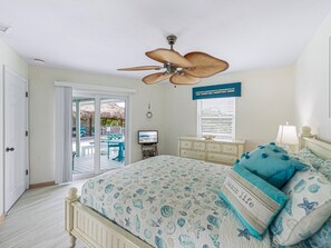 A bedroom with a bed, a ceiling fan, a TV, a dresser, and a window with blinds.