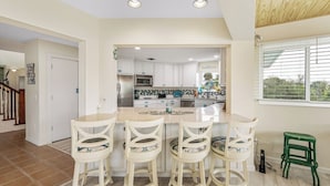 A modern kitchen with white cabinets, a central island with bar stools, and a view of the outdoors through a window.