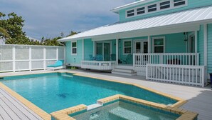 A swimming pool with a deck, a covered patio, and a house with teal siding and white railings.