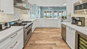 Een moderne keuken met witte kasten, een backsplash in een herringbone patroon, een houten vloer en roestvrijstalen apparatuur.