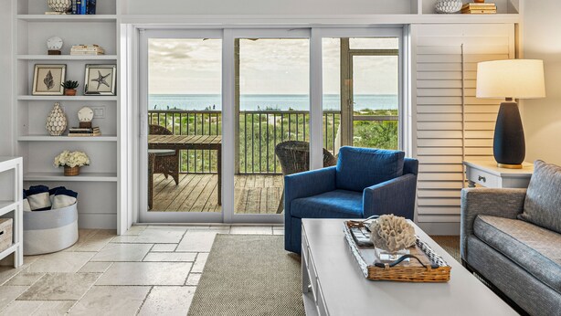 A living room with a view of the ocean, a ceiling fan, and a bookshelf with decorative items. - Sundown 03:  2-bed, 2-bath townhome in Boca Grande stunning Gulf front views, a relaxing getaway. (Boca Grande)