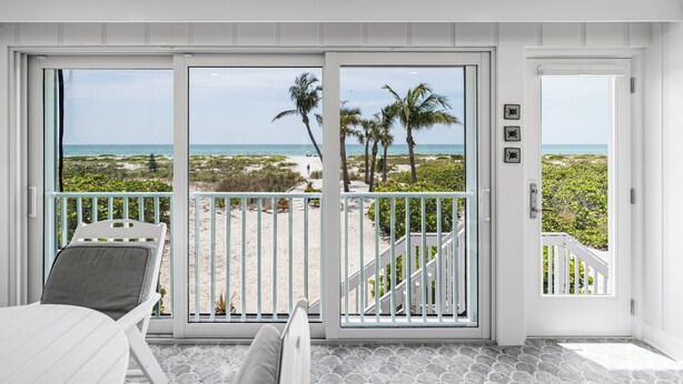 Une chambre avec vue sur la plage, un lit blanc et un balcon avec une balustrade.