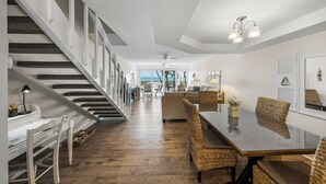 Un vaste espace de vie comprenant un escalier, une table à manger avec des chaises en osier et une vue sur l’océan.
