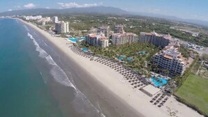 An aerial view of a coastal resort with beachfront hotels, a sandy beach, and a clear blue ocean.