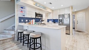 Une cuisine moderne avec des meubles blancs, un îlot central doté de tabourets, un four à micro-ondes, un réfrigérateur et un pare-feu bleu.