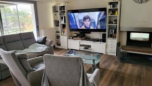 A living room with a flat-screen TV, a fireplace, and a bookshelf. - Weekly rental house with swimming pooleur 5 km from the beach (Plonéour-Lanvern)