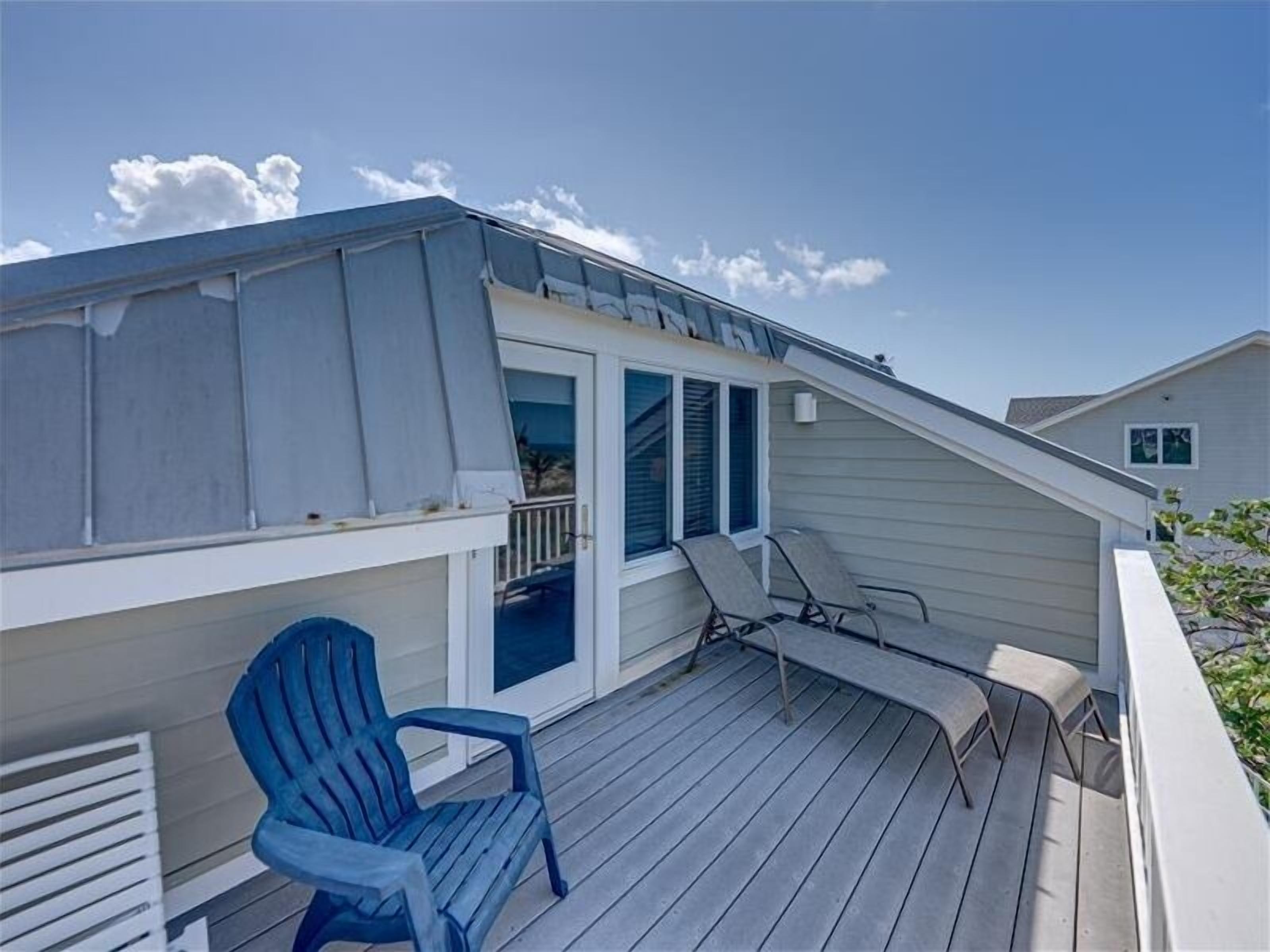 A deck with a blue chair and a table, a covered area with a door, and a clear sky.