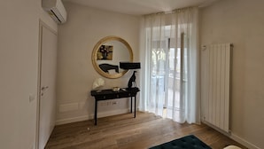 A room with a wooden floor, a black desk with a lamp, a round mirror, and a window with sheer curtains. - Vivaldi Suite (Firenze)