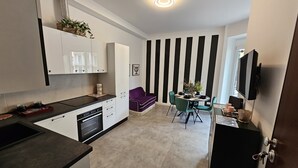 A modern kitchen with white cabinets, a black countertop, and a dining area with a purple sofa and green chairs. - Vivaldi Suite (Firenze)