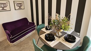 A dining area with a round table, two chairs, a purple sofa, and a black and white striped wall. - Vivaldi Suite (Firenze)