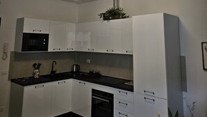 A modern kitchen with white cabinets, a black countertop, a built-in microwave, and a ceiling light fixture. - Vivaldi Suite (Firenze)