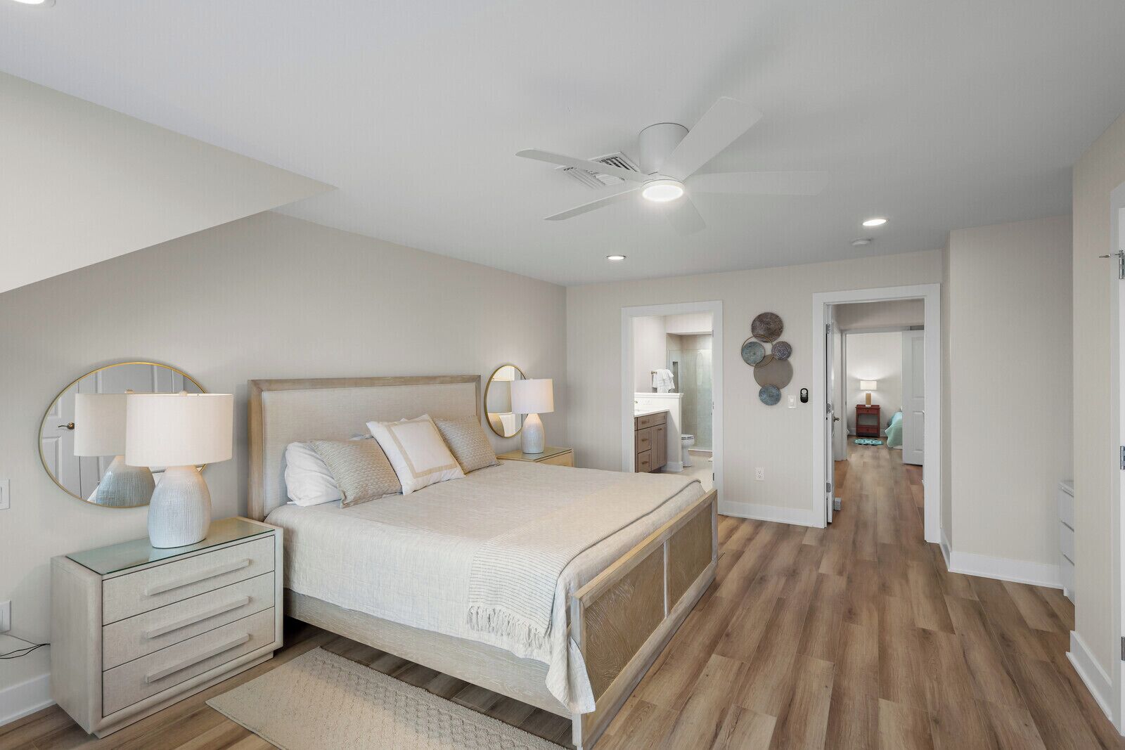 A bedroom with a bed, bedside tables, a ceiling fan, and a view into the bathroom.