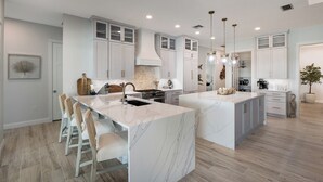 A spacious kitchen with a large island, white cabinetry, and pendant lighting.