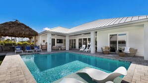 A modern pool area with lounge chairs, a thatched roof structure, and a covered patio.
