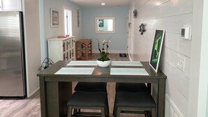 A dining area with a wooden table, two chairs, a potted plant, and a refrigerator.