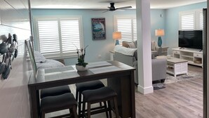 A modern kitchen with a central island, bar stools, a dining table, and a ceiling fan.