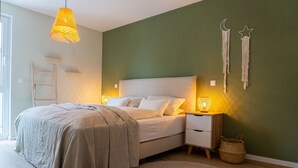 Ett sovrum med en säng, sängbord, ett litet bord, en lampa, en hylla som är monterad på väggen och ett fönster.