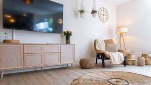 Ett vardagsrum med en platt-TV, möbler i rotting, en rund, flätad pall och en golvlampa.