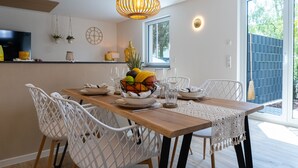 En matplats med ett träbord, vita stolar, en fruktskål och hängande lampor.