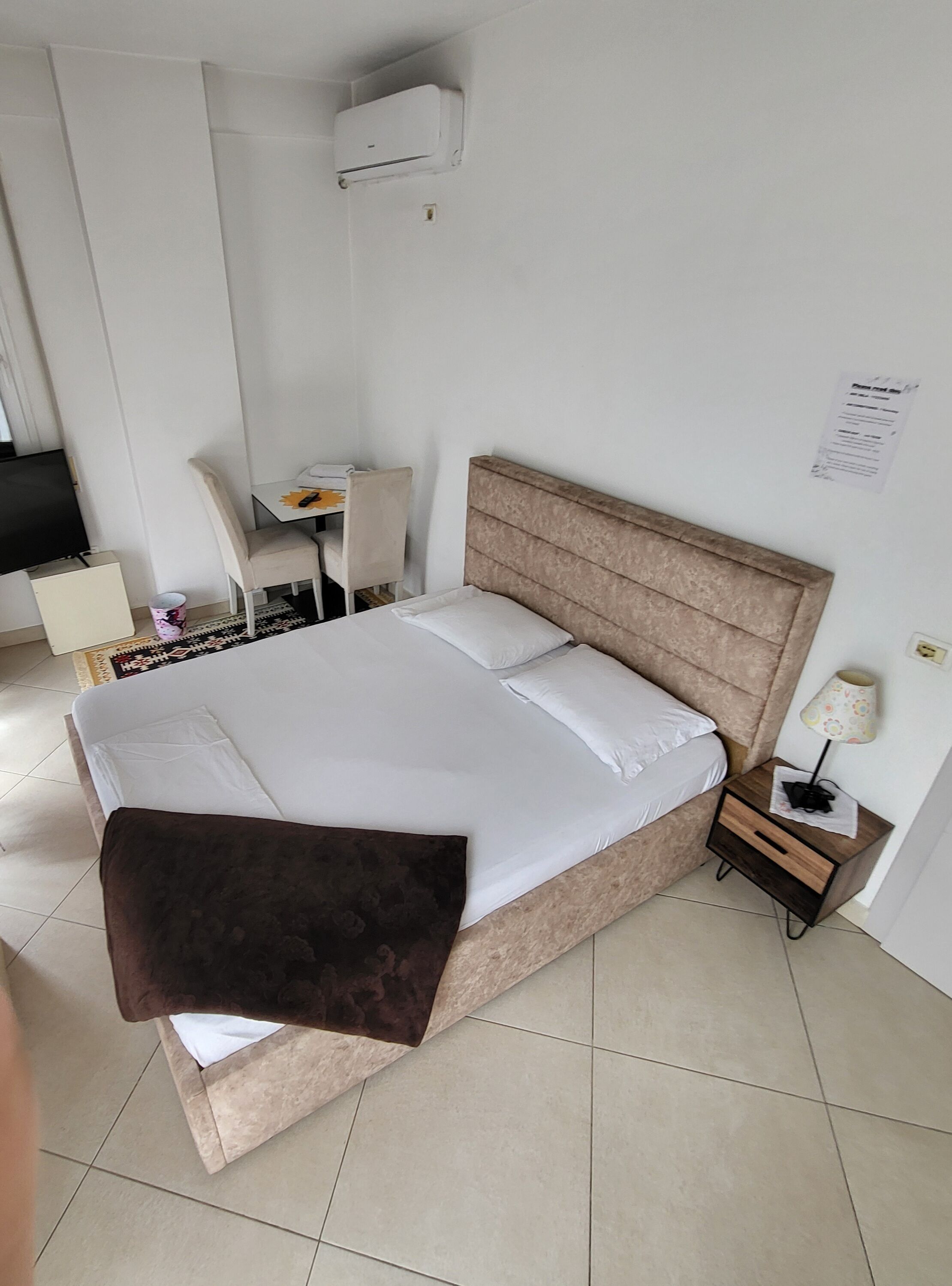 Un dormitorio ordenado con una cama grande, una mesita de noche con lámpara, una silla, un escritorio y un televisor.