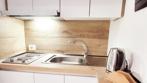 Une petite cuisine équipée d’une cuisinière, d’un évier et d’une bouilloire posée sur le plan de travail.