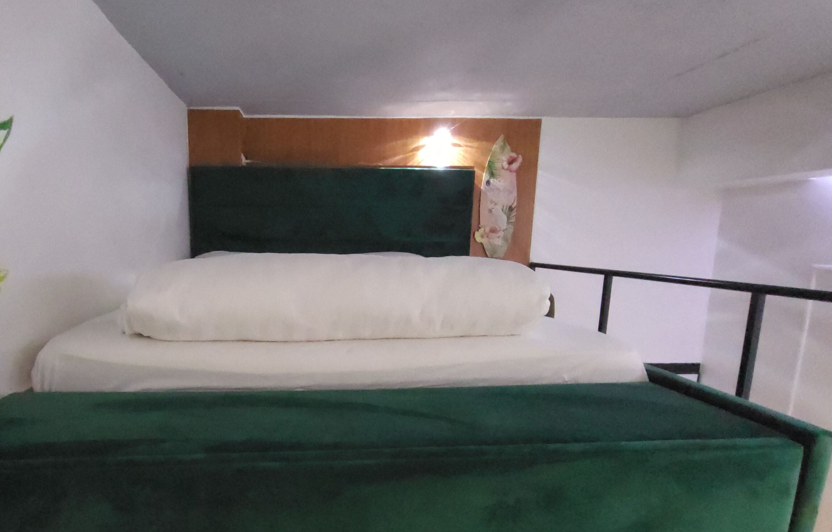 A bed with a green cover, a white pillow, and a headboard with a floral design.