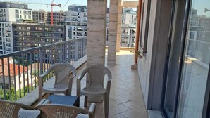 Un balcon avec une table et des chaises, une vue sur les bâtiments environnants et une grue de construction en arrière-plan.