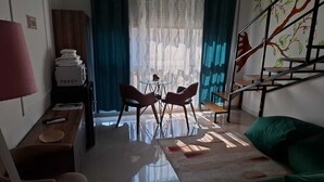 Un salon comprenant un coin repas, un escalier orné d’une fresque représentant un arbre, et une vue sur l’extérieur à travers des rideaux transparents.