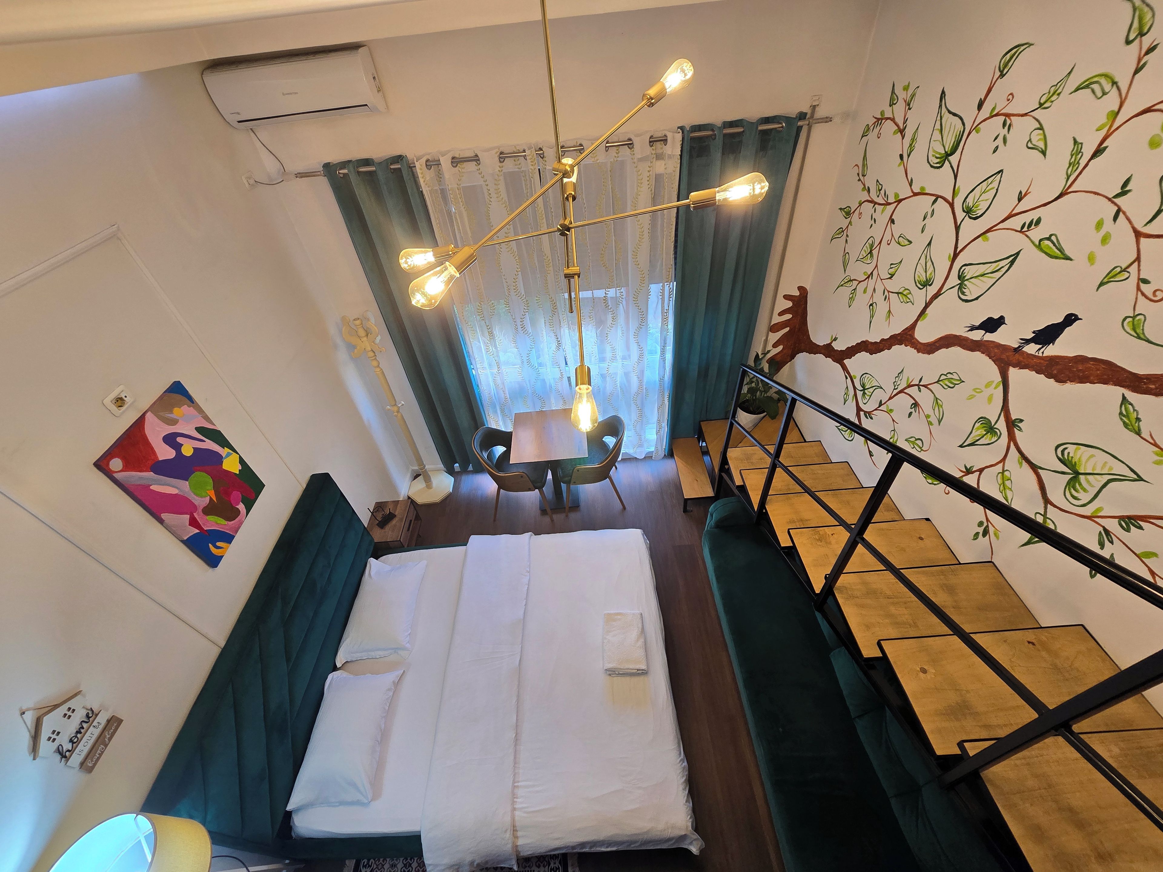 A hotel room with a bed, a desk, a chair, a staircase, and a wall mural.