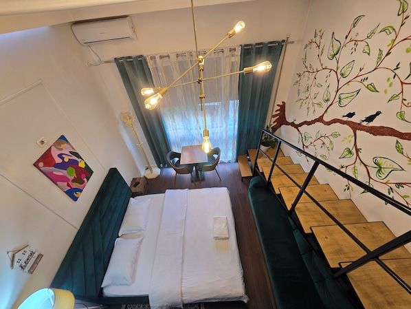 Una habitación de hotel con una cama, un escritorio, una silla, una escalera y un mural en la pared.