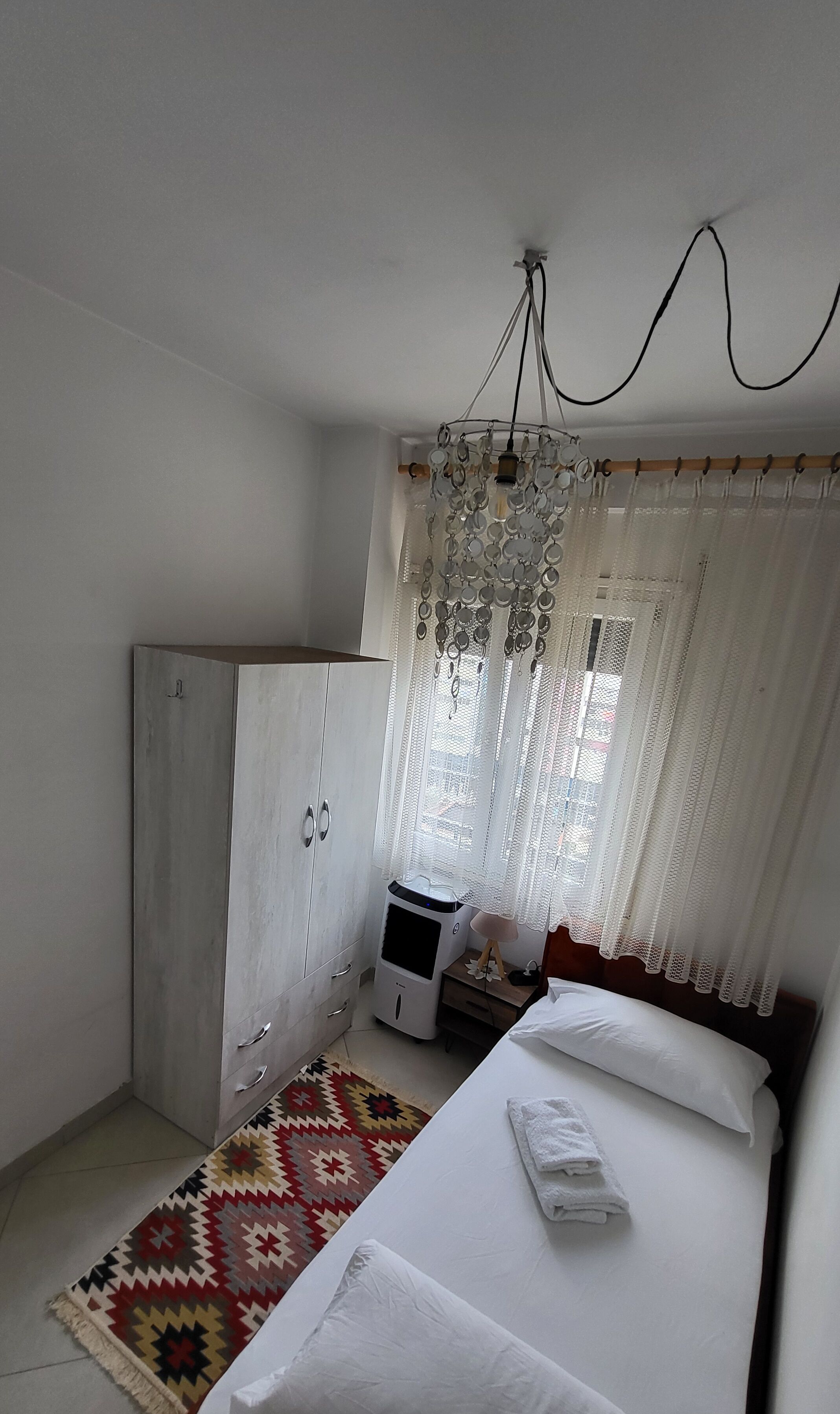 Quarto com cama, guarda-roupa, aquecedor, tapete estampado e cortinas leves.