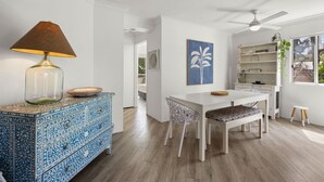 A modern kitchen with white cabinetry, a dining table, and chairs. There is a ceiling fan, a decorative lamp, and a blue wall art piece. - Charming Spacious 2-Bedroom Getaway in Central Burleigh Heads (Gold Coast)