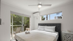 A bedroom with a bed, a ceiling fan, a window, and a view of greenery outside. - Charming Spacious 2-Bedroom Getaway in Central Burleigh Heads (Gold Coast)