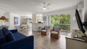 A modern living room with a blue sofa, wicker chairs, a dining area, and a kitchen. - Charming Spacious 2-Bedroom Getaway in Central Burleigh Heads (Gold Coast)