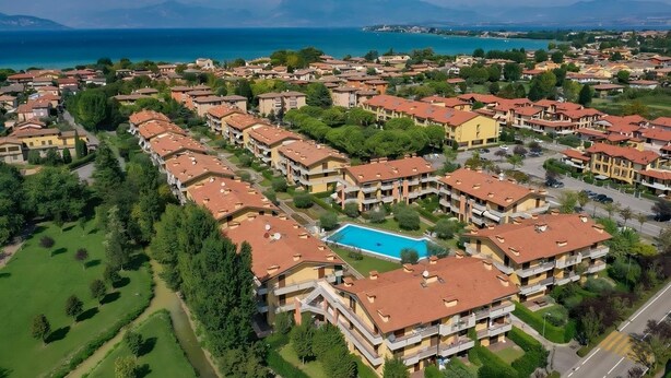 A residential area with apartment buildings, a swimming pool, and a view of the sea. - Villaggio dei Fiori - App Primula (Sirmione)