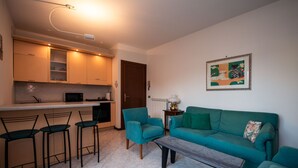 A compact living space with a kitchenette, a sofa, a coffee table, and a dining area with bar stools. - Villaggio dei Fiori - App Primula (Sirmione)