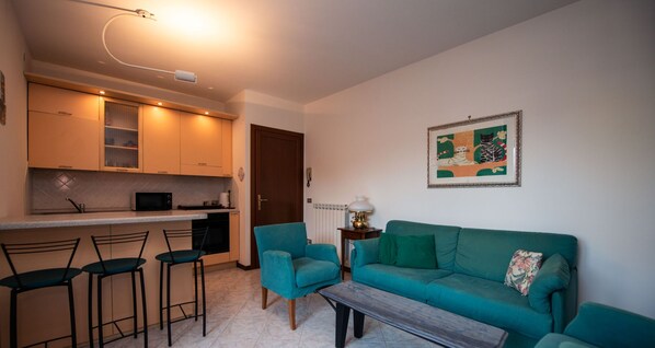 A compact living space with a kitchenette, a sofa, a coffee table, and a dining area with bar stools. - Villaggio dei Fiori - App Primula (Sirmione)