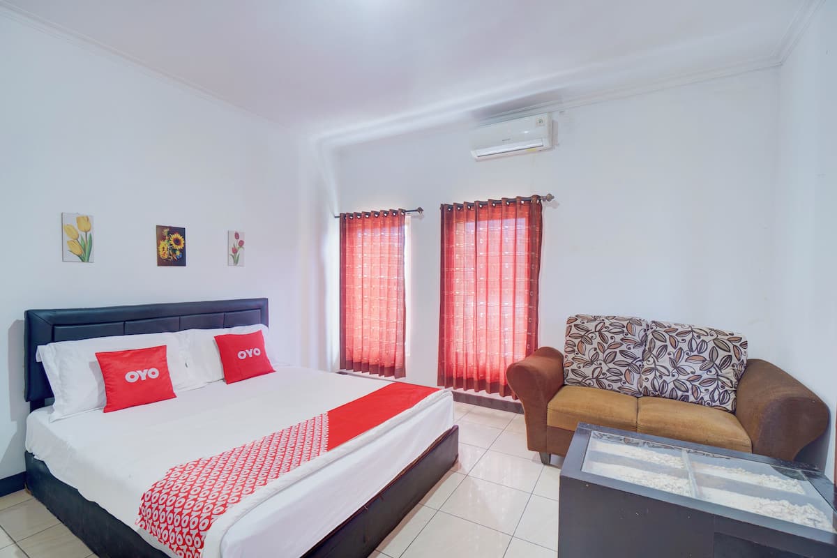 A hotel room with a bed, a sofa, a glass coffee table, and a window with red curtains.