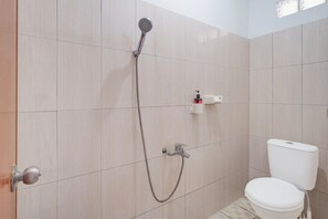 Et badeværelse med bruser, toilet og en lille hylde med en flaske.