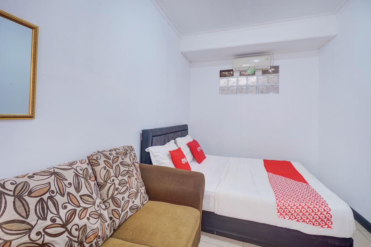 A bedroom with a bed, a brown sofa, and a white wall with a small window.