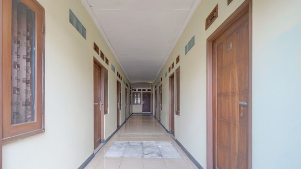 A long, narrow hallway with wooden doors on both sides, leading to a central area. - Hotel O Puncak Bogor Near Taman Safari Formerly Hotel Satya Luhur (Megamendung)