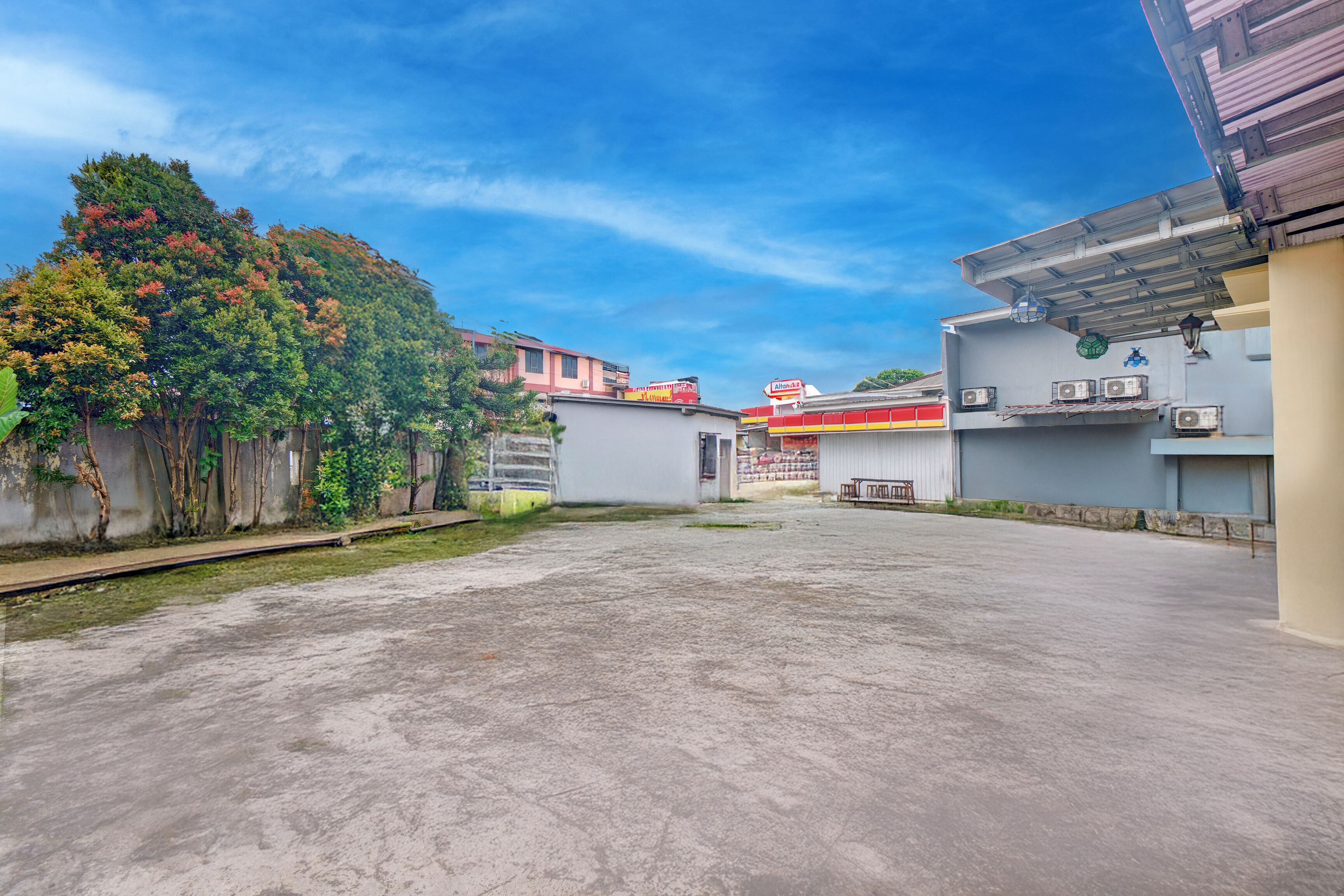 An empty parking lot with a concrete surface, surrounded by buildings, including a gas station with a red and yellow sign.