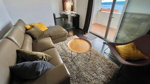 A modern living room with a sofa, a round coffee table, and a chair. There is a view of a balcony through a glass door. - Apartman Jasmin 1 (Crikvenica)