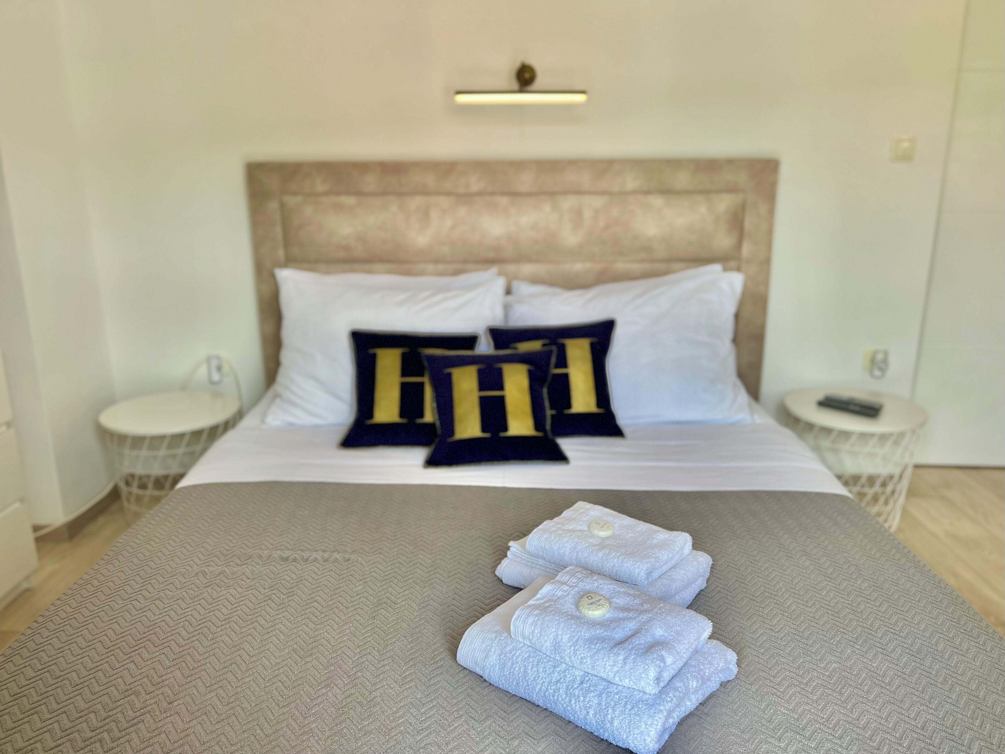 A neatly made bed with a headboard, two pillows with a large letter design, and three folded towels on the bed.