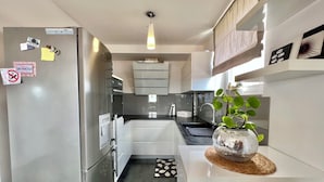 A modern kitchen with a stainless steel refrigerator, built-in oven, and a sink. There is a decorative plant on a woven mat. - Apartman Jasmin 1 (Crikvenica)