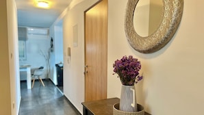 A hallway with a wooden door, a round mirror, and a vase with purple flowers on a dark wooden table. - Apartman Jasmin 1 (Crikvenica)